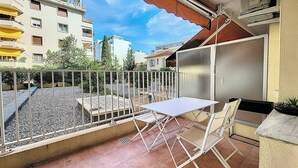 A balcony with a white table and chairs, a metal railing, and a view of neighboring buildings. - HENRI CAMILLE AGENCY - Bosquets - Studio w/ terrace close center (Cannes)