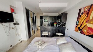 A modern hotel room with a large bed, a TV mounted on the wall, a kitchen area, and a bathroom. - HENRI CAMILLE AGENCY - Bosquets - Studio w/ terrace close center (Cannes)