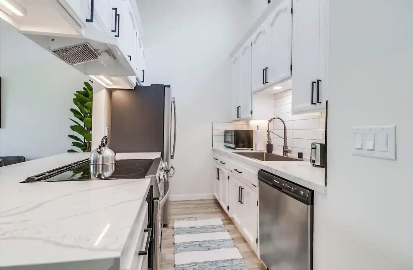 A narrow kitchen with white cabinets, a stainless steel refrigerator, a microwave, and a dishwasher.