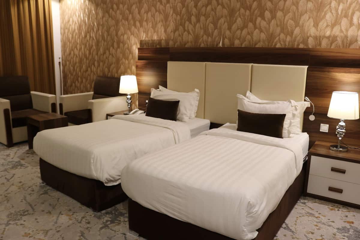 Een hotelkamer met twee bedden, een bureau, een stoel, een lamp en een telefoon.
