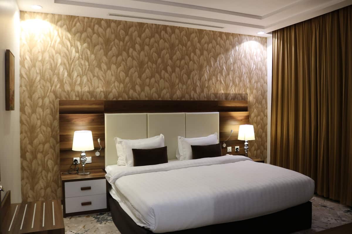 Een hotelkamer met een groot bed, twee nachtkastjes met lampen, een houten hoofdbord en behang met een patroon.