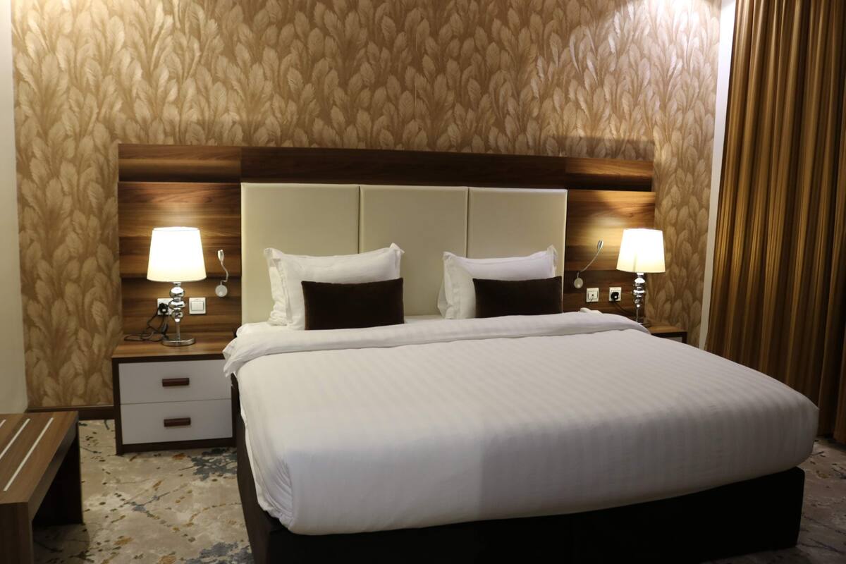 Een hotelkamer met een groot bed, twee nachtkastjes met lampen, een houten hoofdbord en behang met een patroon.