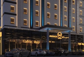 Un hôtel avec un café situé au rez-de-chaussée, plusieurs voitures garées devant et des fenêtres illuminées.
