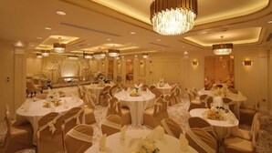 A banquet hall with round tables, gold chairs, and chandeliers.
