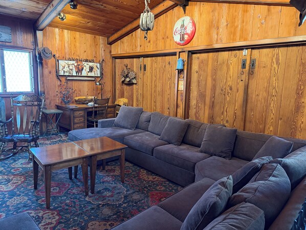 A wooden interior with a sectional sofa, a table, and a patterned rug. - Beautiful & Spacious 7-Beds by 𝐁𝐘𝐔𝐈 (Rexburg)