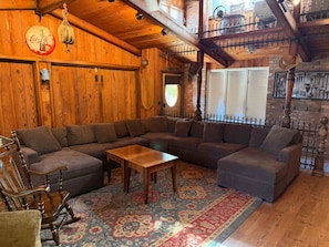 Ein gemütliches Holzinterieur mit einem Ecksofa, einem Schaukelstuhl und einem gemusterten Teppich.