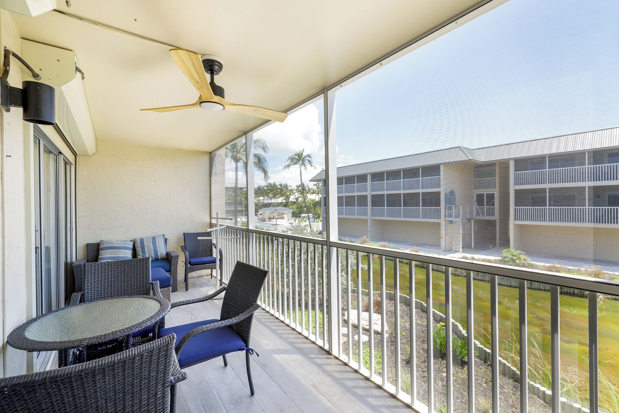 A balcony with wicker furniture, a glass table, and a ceiling fan.