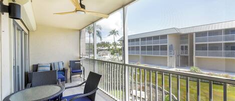 A balcony with wicker furniture, a glass table, and a ceiling fan.
