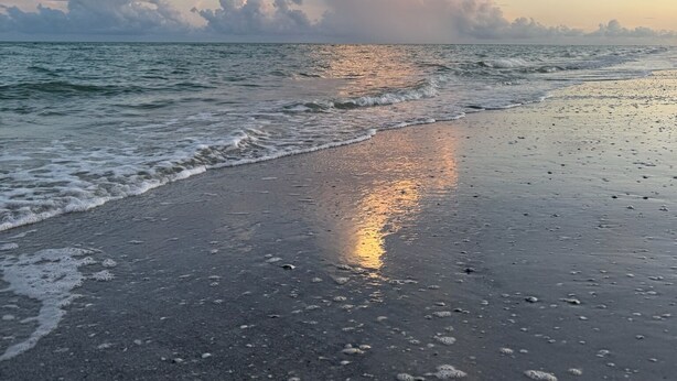 En strand med ett lugnt hav, en klar himmel och några få moln.