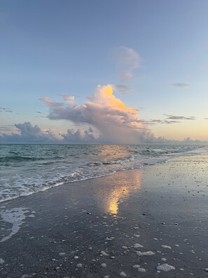 Ein Strand mit ruhiger See, blauem Himmel und vereinzelten Wolken.