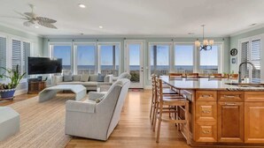 A spacious living room with a large sofa, a dining area with wooden chairs, and a kitchen with wooden cabinets. - 6br Oceanfront Cottage w/ awesome views and short walk to the boardwalk. (Carolina Beach)