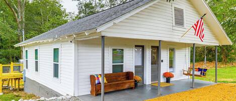 Une maison blanche d’un seul étage, dotée d’un porche, d’une chaise suspendue et d’un banc.
