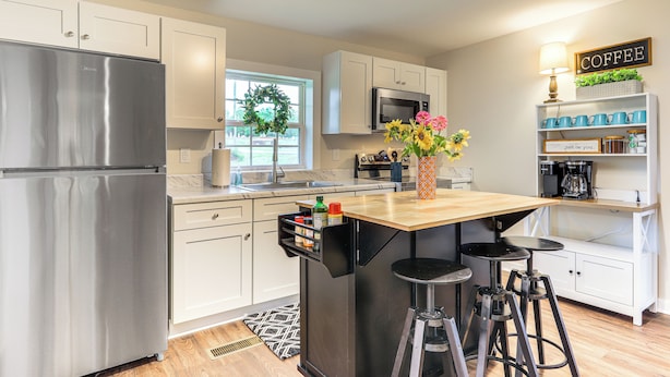 A modern kitchen with stainless steel appliances, a central island with stools, and a coffee station. - Downtown Heflin Cottage w/ Deck & Fire Pit! (Heflin)