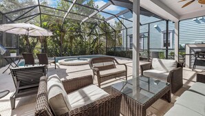 A covered outdoor patio with wicker furniture, a glass table, and a pool. - Patriot's Peaceful Retreat: Private Pool, Free Water Park, Near Disney (Kissimmee)