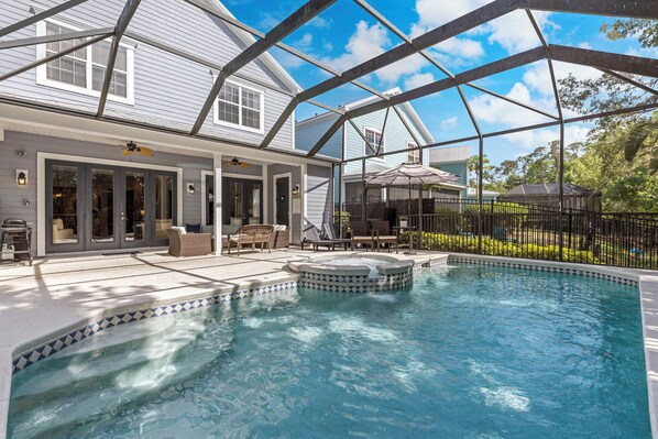 A swimming pool with a hot tub, surrounded by a covered patio area with outdoor furniture.