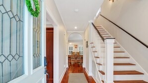 A hallway with wooden flooring, a white door with glass panels, and a staircase with white railings.