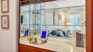 A bathroom with a large mirror, a vanity with a sink, and a shelf with books.