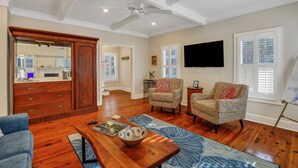 A spacious living room with hardwood floors, a ceiling fan, a large mirror, and a television.
