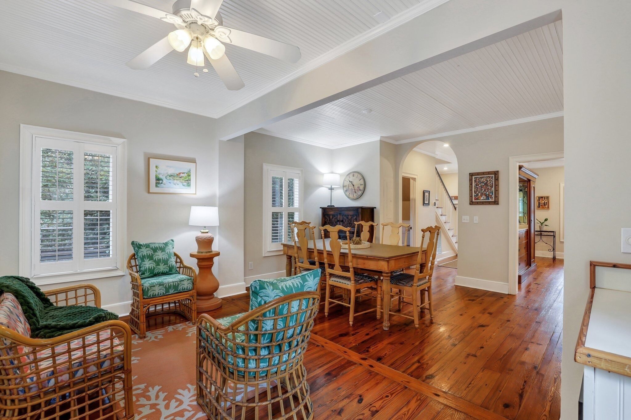 A spacious living room with a wooden floor, wicker furniture, and a dining area with a wooden table and chairs.