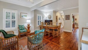 A spacious living room with a wooden floor, wicker furniture, and a dining area with a wooden table and chairs.