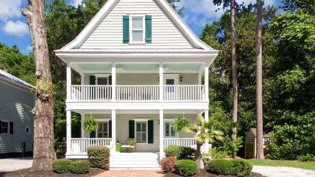 A two-story white house with green shutters, a front porch, and a small garden.