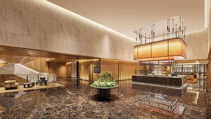 Een ruime lobby met een centraal receptiegedeelte, een zithoek met een groene bank en een decoratieve plantencompositie.