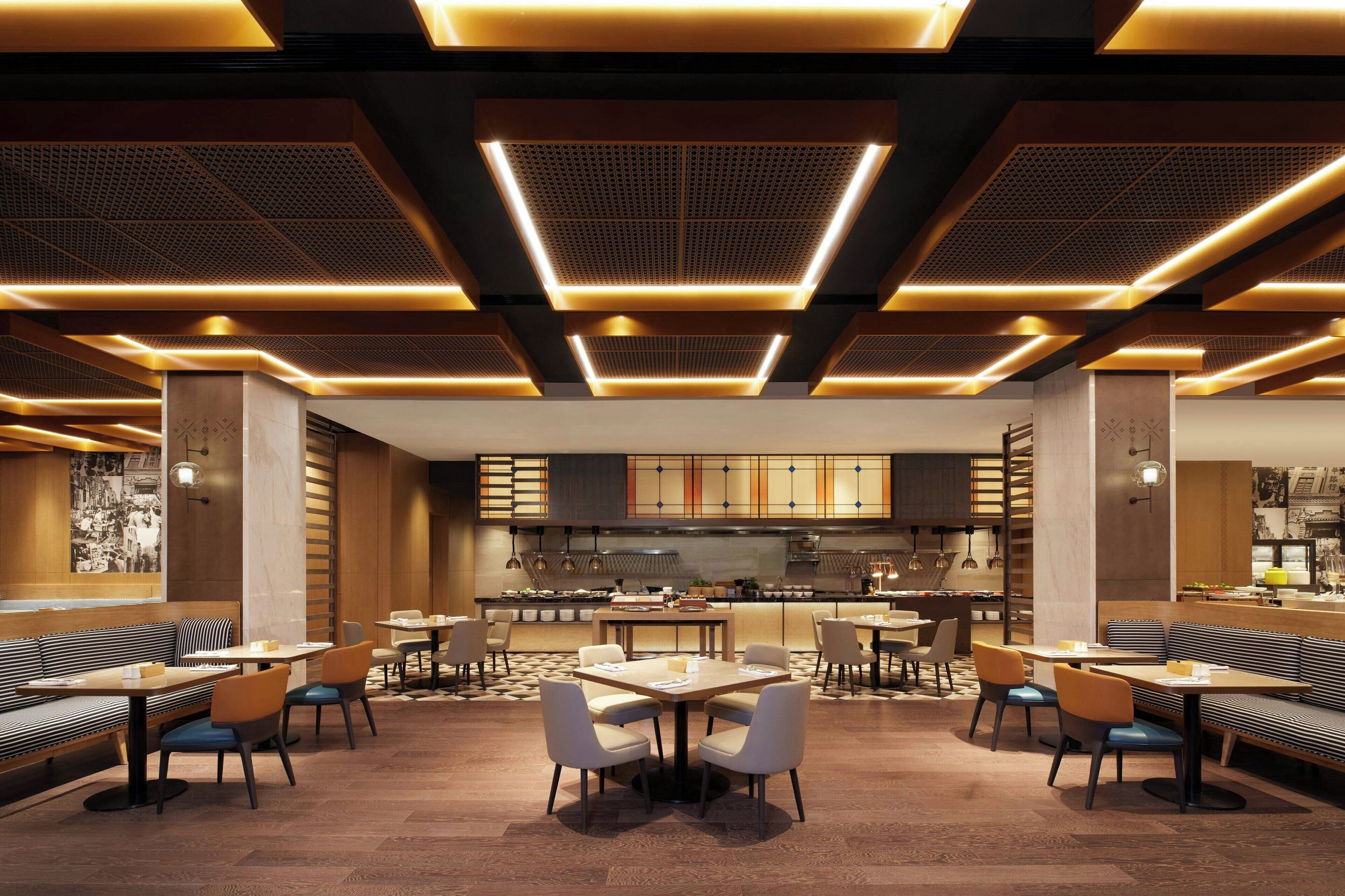 A modern restaurant with a central dining area, booths, and a kitchen in the background.