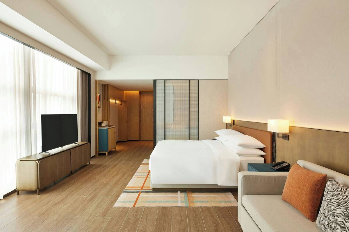 Ein Hotelzimmer mit einem großen Bett, einer Couch, einem Fernseher, einem Schreibtisch und einem großen Fenster.