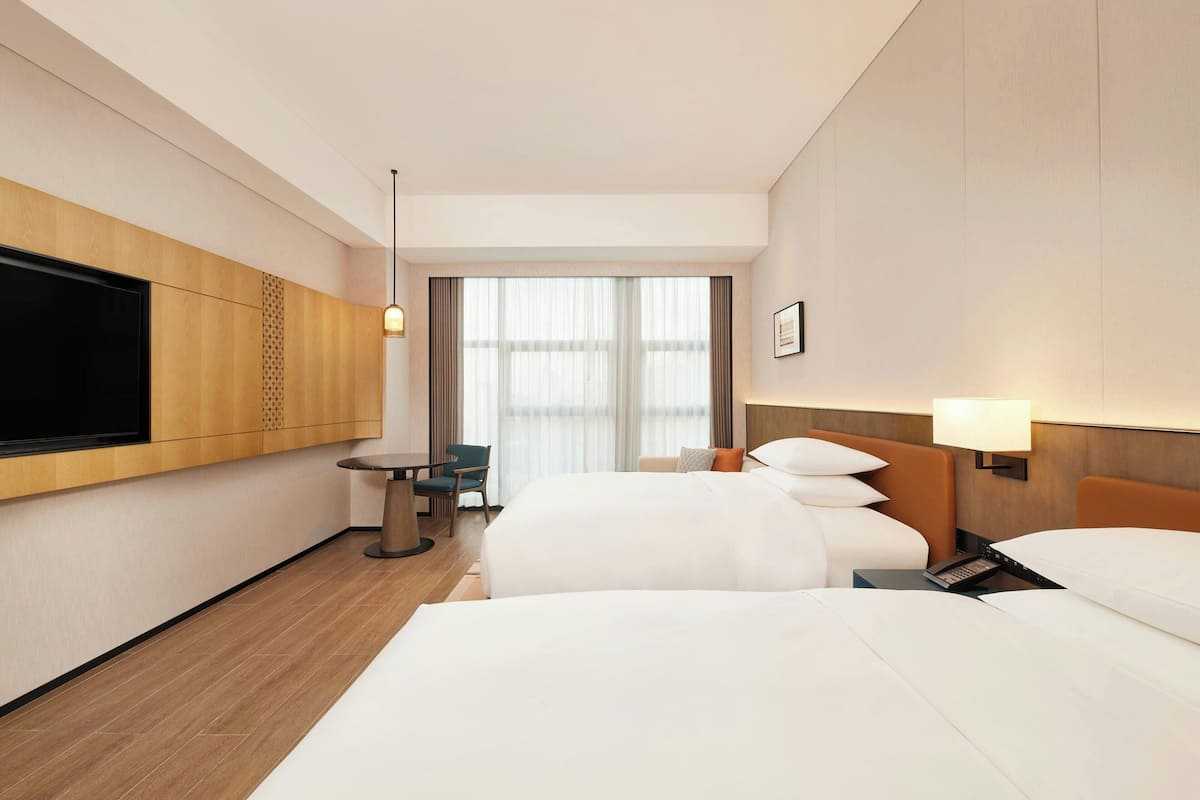 Ein Hotelzimmer mit zwei Betten, einem Fernseher, einem kleinen Tisch und einem Stuhl.