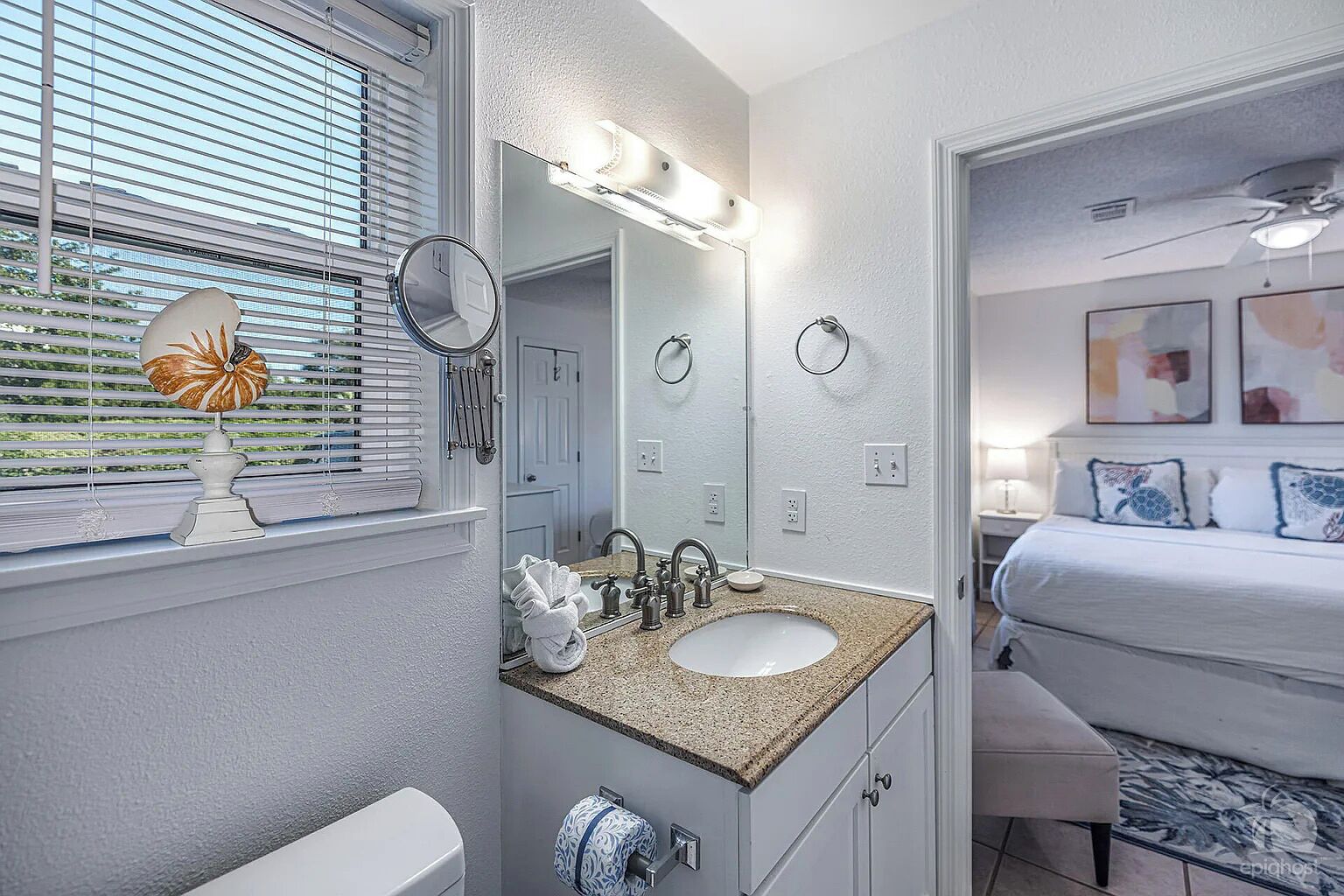 A bathroom with a sink, mirror, and towel rack. There is a window with blinds and a towel hanging on the rack.
