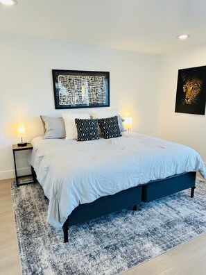Une chambre à coucher comprenant un lit, deux tables de chevet, un tapis et des œuvres d’art murales.
