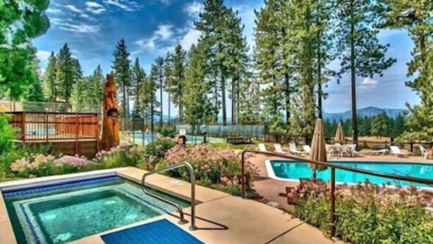 A pool area with a hot tub, lounge chairs, and a wooden deck surrounded by trees. - Mountain Views Condo | Community Pool & Hot Tub (Zephyr Cove)
