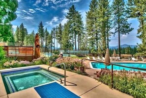 A pool area with a hot tub, lounge chairs, and a wooden deck surrounded by trees. - Mountain Views Condo | Community Pool & Hot Tub (Zephyr Cove)