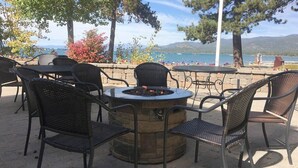An outdoor seating area with a circular fire pit table surrounded by chairs, overlooking a body of water and mountains. - Steps to Beach | Deck | Community Pool & More (South Lake Tahoe)
