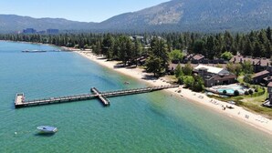 A coastal area with a pier extending into clear water, a beach with sun loungers, and a backdrop of mountains. - Steps to Beach | Deck | Community Pool & More (South Lake Tahoe)