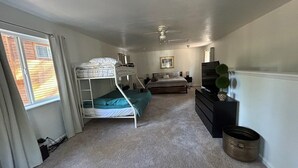 Un dormitorio con literas, una cama, un aparador, un ventilador de techo y una ventana con cortinas.