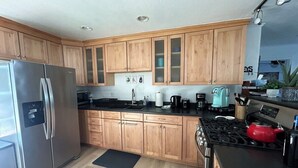 Cocina moderna con armarios de madera, un refrigerador de acero inoxidable, una estufa a gas y un hervidor rojo.