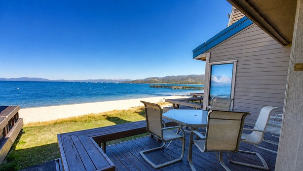 A wooden deck with a table and chairs, overlooking a beach and the ocean.
