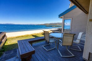 Une terrasse en bois avec une table et des chaises, donnant sur une plage et l’océan.