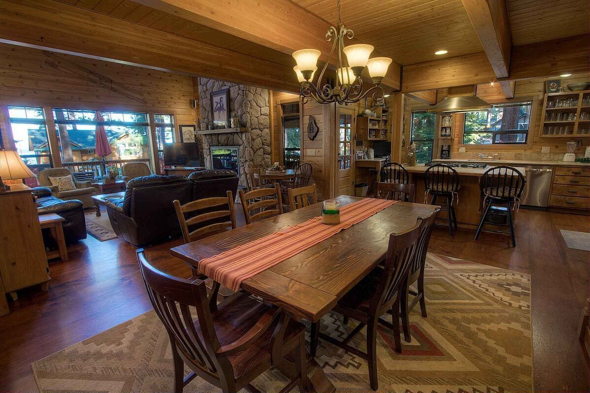 Une cuisine spacieuse avec des meubles en bois, un coin repas doté d’une longue table et un salon confortable avec une cheminée.