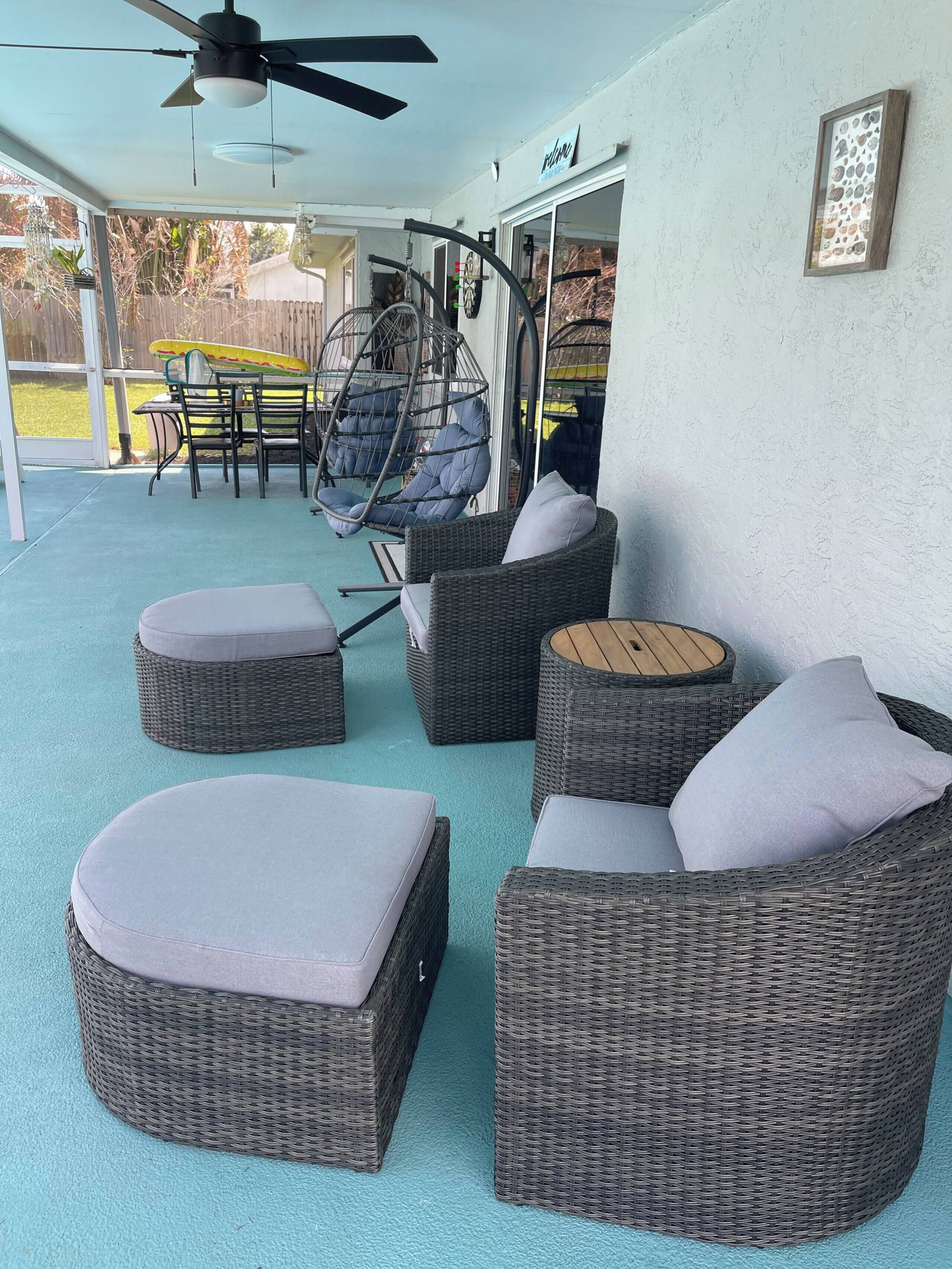 Un patio techado con mobiliario de mimbre, incluyendo sofás y una mesa, y una silla colgante.