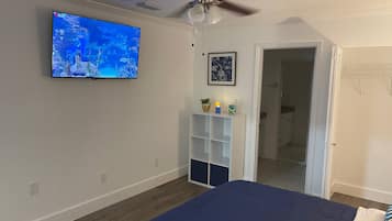 A bedroom with a bed, a ceiling fan, a TV on the wall, a door, and a small shelf with decorative items.
