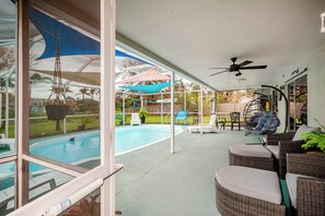 Ein überdachter Außenbereich mit Pool, Sitzgelegenheiten und Deckenventilator.