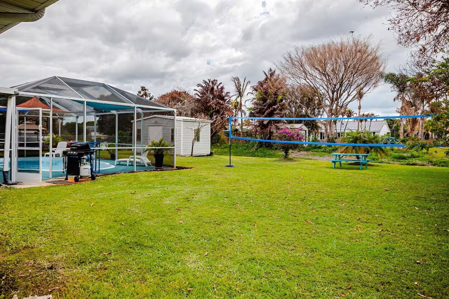 Un patio trasero con piscina, un porche cubierto y una mesa de picnic.