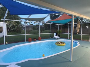 Un patio arrière aménagé, doté d’une piscine, d’un radeau de style tiki et de mobilier d’extérieur.