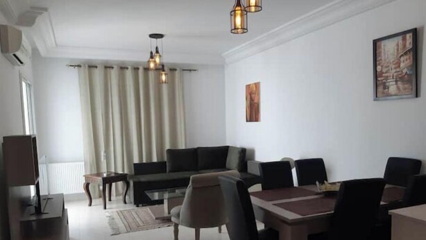 A modern living room with a sofa, dining table, chairs, and a TV.