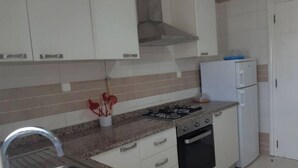 A compact kitchen with white cabinets, a gas stove, a built-in oven, and a white refrigerator.