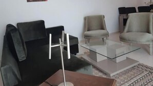A living room with a black sofa, a glass coffee table, and two beige armchairs.