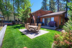 A wooden house with a patio, a barbecue area, and a lawn.