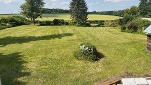 A well-maintained lawn with a wooden bench and a small table, surrounded by trees and a distant view of a field. - Beautiful old rustic house on two acres of overlooking fields in the back garden (Winchester)